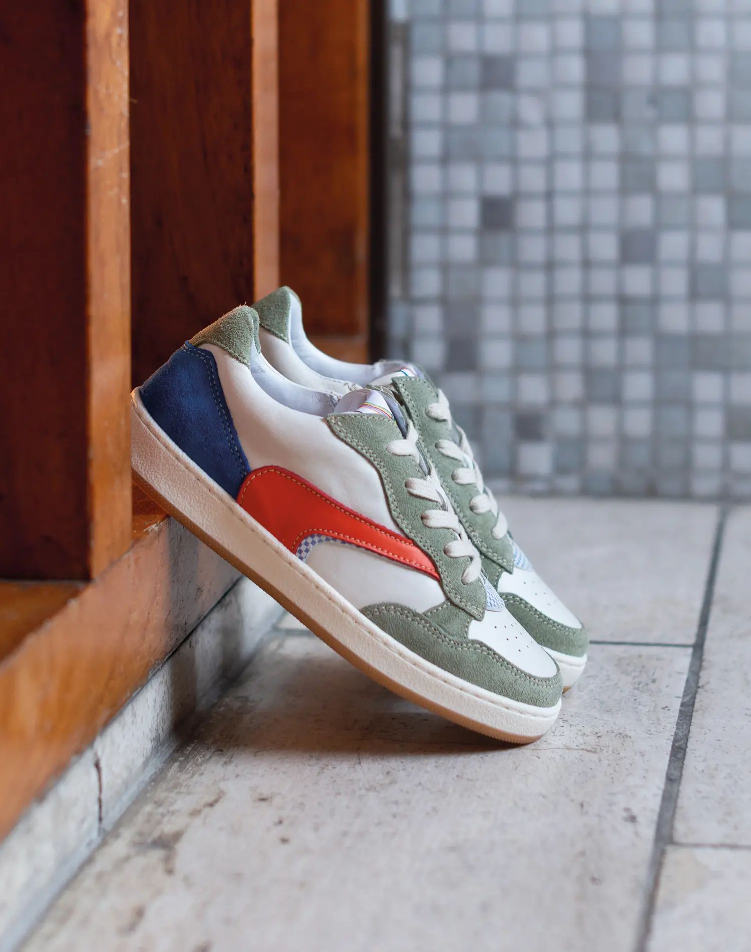 Sportieve kinder sneaker met rood detail op tegelvloer